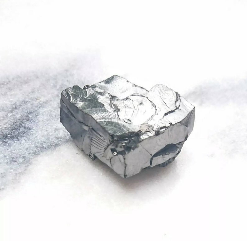 May include: A rough, gray, metallic rock with a crystalline structure. The rock has a jagged, irregular shape and appears to be a raw mineral specimen.