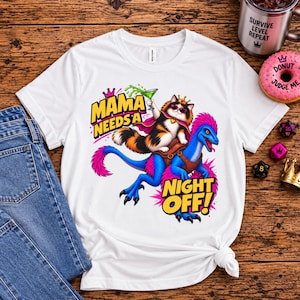 Puede incluir: Una camiseta blanca con el gráfico de un gato calicó con corona y gafas de sol, montado sobre un dinosaurio azul con plumas rosas. El gato sostiene un cóctel verde. El texto dice MAMA NEEDS A NIGHT OFF en letras amarillas y negras.