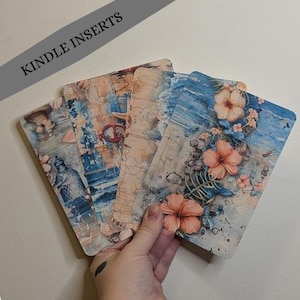 May include: A collection of Kindle inserts with watercolor designs. The inserts feature a variety of patterns, including floral, abstract, and nautical themes. The color palette includes blues, oranges, and tans. The text "KINDLE INSERTS" is visible.