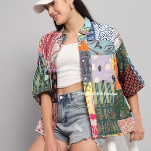 May include: A colourful patchwork shirt with various patterns, including paisley and floral designs. The shirt has short sleeves and a button-up front. The model is wearing a white cap and denim shorts.