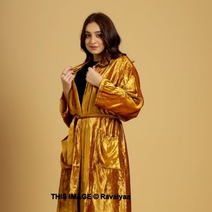 May include: A long, mustard yellow velvet robe with a tie belt and two patch pockets. The robe is worn by a person with long brown hair and is standing on a light brown background. The text "THIS IMAGE © Ravaliyaaa" is at the bottom of the image.