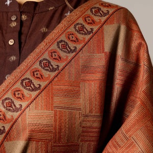 May include: A brown and beige shawl with a geometric pattern and paisley border. The shawl is made of a soft, woven fabric.