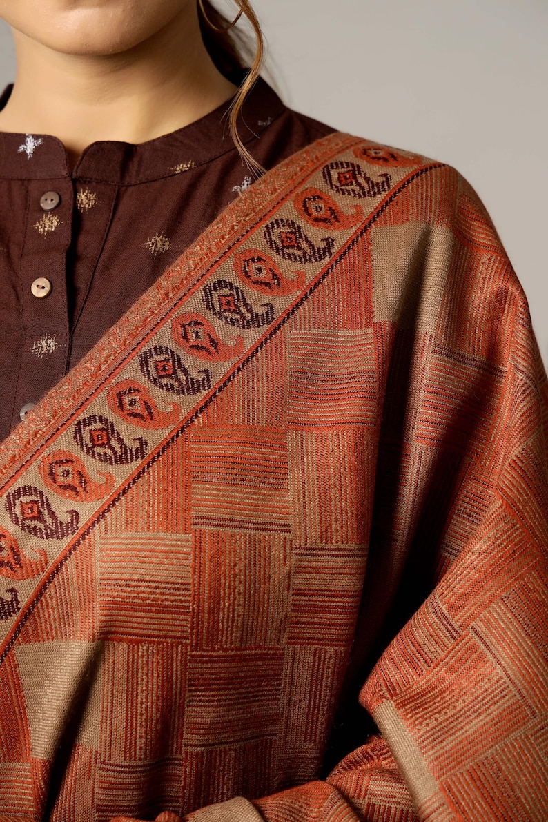 May include: A brown and beige shawl with a geometric pattern and paisley border. The shawl is made of a soft, woven fabric.