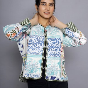 Puede incluir: Una chaqueta acolchada blanca con estampado floral y ribete verde. La chaqueta tiene cierre de botón y mangas largas.