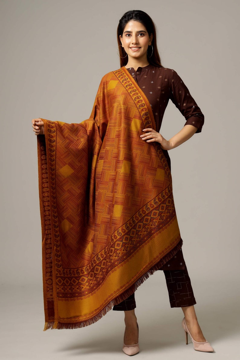May include: A mustard yellow shawl with a geometric pattern and a maroon border. The shawl has a fringe trim and is made of a soft, luxurious fabric.