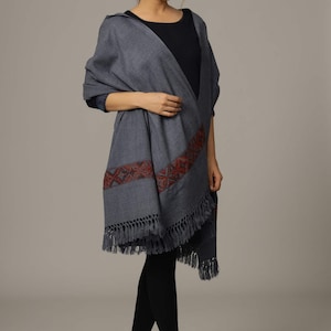 May include: A gray shawl with a red and blue embroidered border and fringe. The shawl is draped over a person's shoulders.