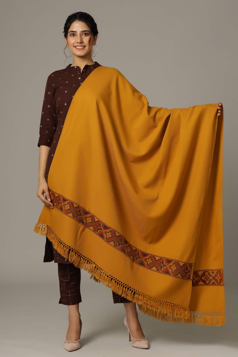 May include: A mustard yellow shawl with a brown and orange embroidered border and fringe.