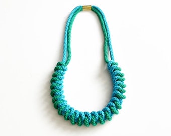 May include: A blue and green rope necklace with a gold clasp. The rope is twisted into a spiral pattern.