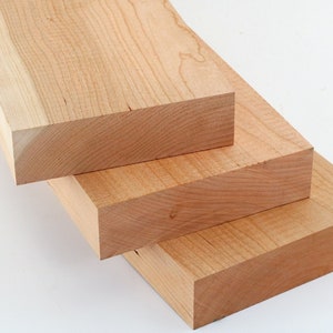 May include: Three pieces of unfinished, light brown wood stacked on top of each other. The wood has a smooth, natural grain.