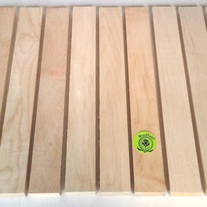 May include: Ten pieces of unfinished, light brown wood strips. The strips are approximately 1/2 inch wide and 12 inches long. The wood is smooth and has a natural grain pattern. The strips are arranged in a row on a white surface. The text "WoodNeck" is visible on a green circle sticker.