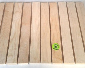 Peut inclure: Dix morceaux de bois brut de couleur brun clair. Les lattes mesurent environ 1,2 cm de large et 30 cm de long. Le bois est lisse et présente un grain naturel. Les lattes sont disposées en rangée sur une surface blanche. Le texte "WoodNeck" est visible sur un autocollant rond vert.