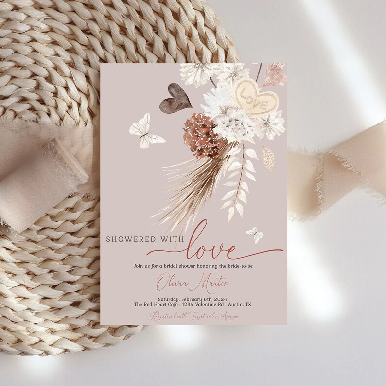 May include: A blush pink bridal shower invitation with a watercolor illustration of dried flowers, butterflies, and a heart with the word "Love" on it. The text reads "Showered with love" and includes the bride-to-be's name, the date, location, and registry information.