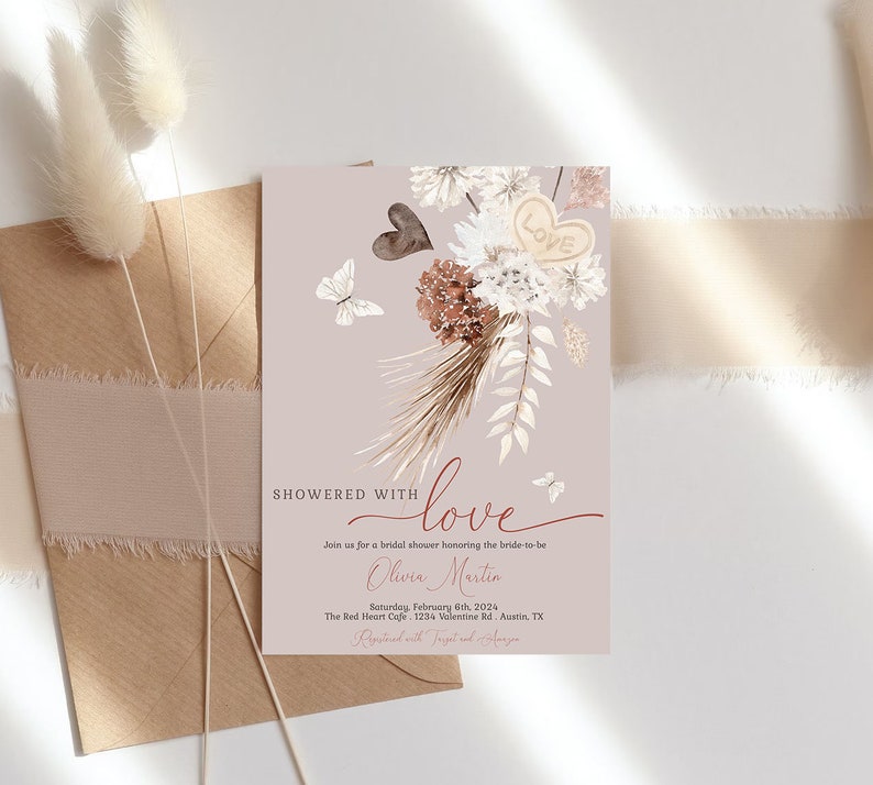 May include: A blush pink bridal shower invitation with a watercolor illustration of a bouquet of dried flowers, butterflies, and a heart with the word "love" on it. The text "Showered with love" is written in a script font. The invitation includes the bride-to-be's name, the date, time, and location of the shower.