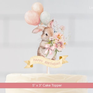 Op de afbeelding: Een aquarel taarttopper met een bruin konijn met bloemen en een roze strik, met drie pastelkleurige ballonnen. Een banner leest "Happy Birthday!" De topper is 12,7 cm x 7,6 cm groot.