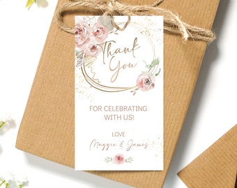 May include: White thank you tag with gold glitter and a gold circle frame with the words "Thank You" in gold script. The tag has a watercolor floral design with pink flowers and green leaves. The text "For celebrating with us! Love Maggie & James" is printed below the frame.