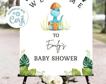 May include: A baby shower welcome sign featuring a blue dinosaur hatching from an egg, surrounded by green leaves. The sign reads "WELCOME TO Emily's BABY SHOWER". The sign is displayed on a black easel.