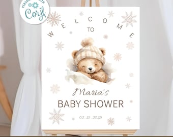 Może przedstawiać: Znak powitalny na baby shower z akwarelową ilustracją misia w zimowej czapce. Znak zawiera tekst "Witamy na baby shower Marii" i datę 02.15.2025, z akcentami płatków śniegu.