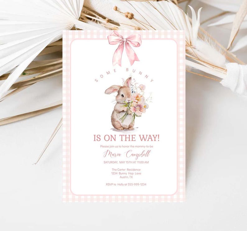 May include: Pink and white gingham baby shower invitation with a watercolor illustration of a brown bunny holding a bouquet of pink flowers. The text reads "Some Bunny is on the Way!" and includes the name Maria Campbell, the date and time of the event, and the location.
