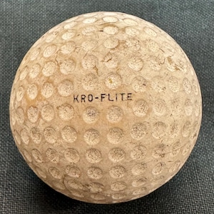 May include: A close-up of a white golf ball with the text "KRO-FLITE" printed on it.