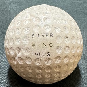 May include: A white golf ball with the words "SILVER KING PLUS" embossed on it.