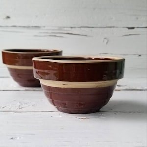 May include: Two brown and white ceramic bowls with a glazed finish. The bowls are small and have a rounded shape.