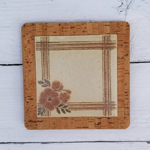 Puede incluir: Un posavasos cuadrado con respaldo de corcho y una baldosa beige con un diseño floral y rayas marrones. La baldosa está rodeada por un marco de corcho.
