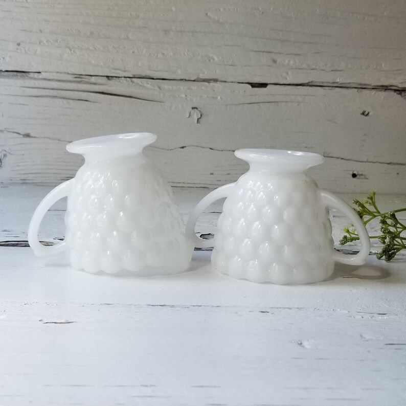 May include: Two white milk glass creamer pitchers with a textured bubble design and handles.