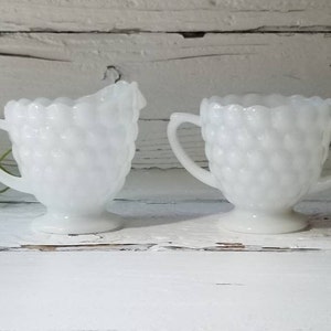 May include: A set of two white milk glass creamer and sugar bowls with a textured, raised bubble design.