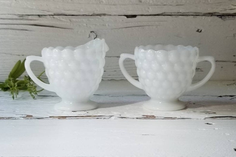 May include: A set of two white milk glass creamer and sugar bowls with a textured, raised bubble design.