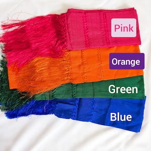 May include: Four rectangular scarves with fringe ends, stacked vertically in pink, orange, green, and blue. Each scarf features a textured woven pattern and is labeled with its respective color name in a box on the right side of the image.