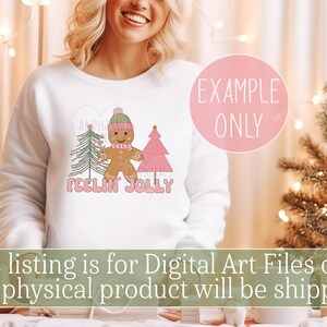 May include: A white sweatshirt with a pink heart design featuring a gingerbread man, two Christmas trees, and the text "Feelin' Jolly".