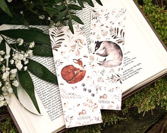 May include: Two illustrated bookmarks with watercolor designs of a fox and a badger in a forest setting. The bookmarks feature a white background with brown, green, and gray illustrations. The text "FUCHS MAERCHEN" is printed on the bottom of each bookmark.
