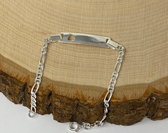 Puede incluir: Un brazalete de plata con una etiqueta rectangular que tiene un recorte en forma de corazón. El brazalete tiene un estilo de cadena figaro.