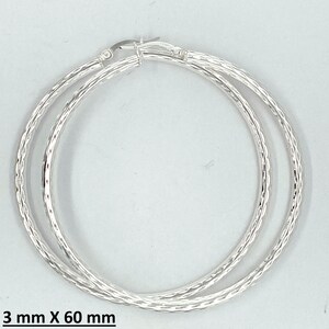 May include: Silver hoop earrings with a textured design. The earrings are 3 mm wide and 60 mm in diameter.