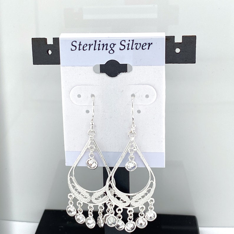 May include: Sterling silver dangle earrings with a teardrop design and clear crystal accents. The earrings have a delicate filigree pattern and are hanging from a hook.