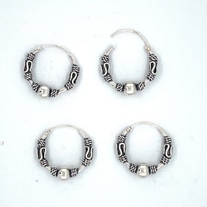 May include: Four silver hoop earrings with a small bead and decorative details. The earrings are arranged in a square pattern on a white background.