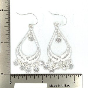 May include: Silver dangle earrings with a teardrop design and clear crystal accents. The earrings are approximately 2 inches long.