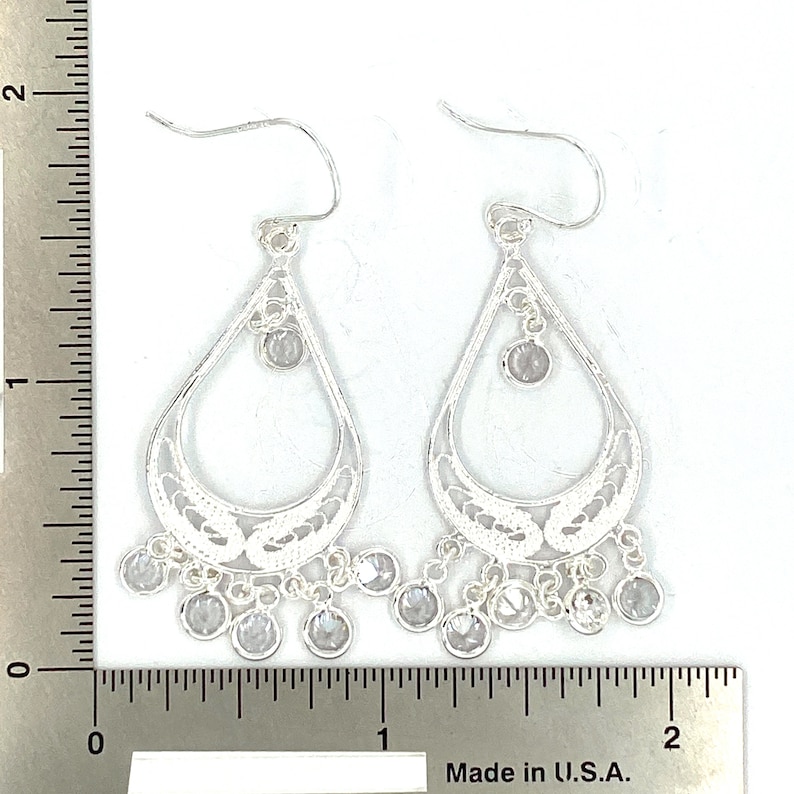 May include: Silver dangle earrings with a teardrop design and clear crystal accents. The earrings are approximately 2 inches long.
