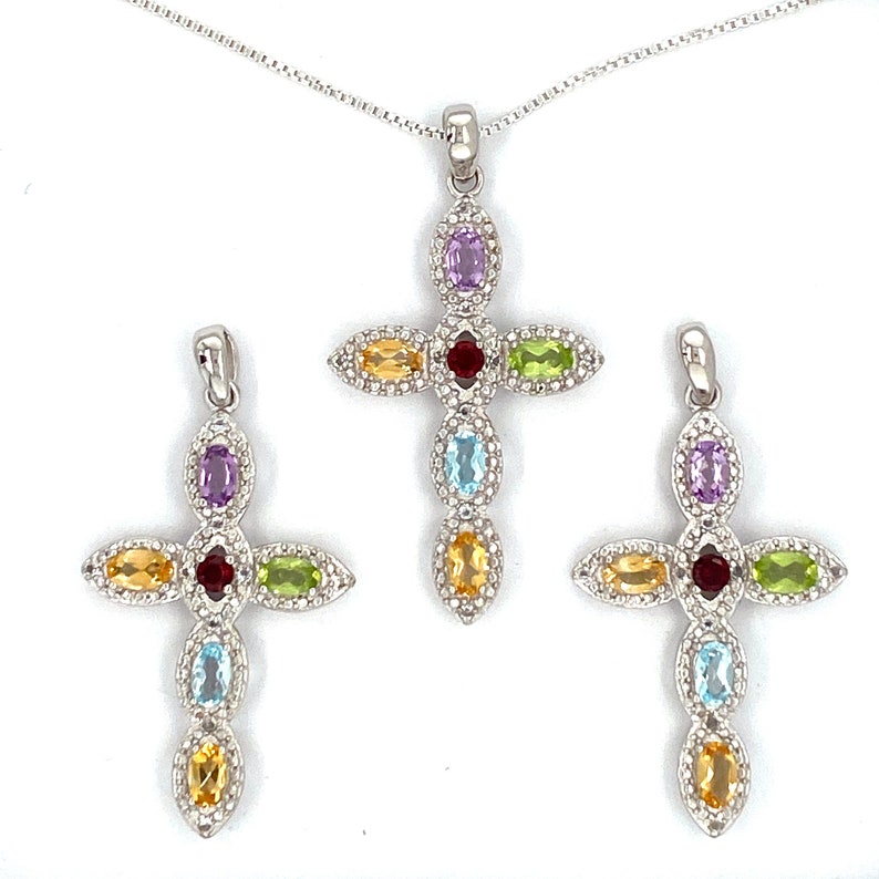 Puede incluir: Tres colgantes de cruz de plata con piedras preciosas de colores. Cada cruz presenta una piedra preciosa roja central rodeada de piedras preciosas m&aacute;s peque&ntilde;as en tonos de amarillo, verde, azul y morado.