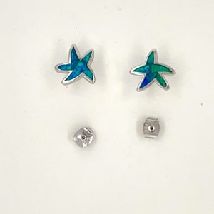 May include: A pair of silver starfish earrings with blue and green opal inlays. The earrings are shown with their backs.