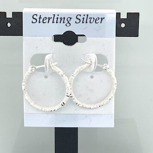 May include: Sterling silver hoop earrings with a textured finish. The earrings are displayed on a white card with the text "Sterling Silver".
