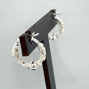 May include: Silver hoop earrings with a textured design and a small ball charm.