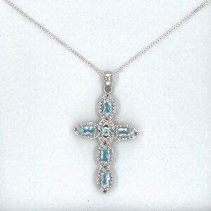 Puede incluir: Un collar de cadena de plata con un colgante de cruz con cinco piedras de topacio azul ovaladas.