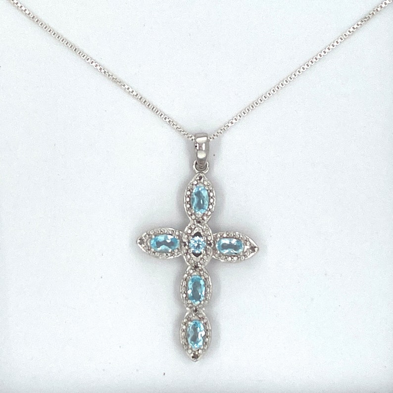 Puede incluir: Un collar de cadena de plata con un colgante de cruz con cinco piedras de topacio azul ovaladas.