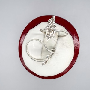 May include: Silver ring with a butterfly design featuring clear rhinestones. The ring is displayed on a red and white ring display stand.