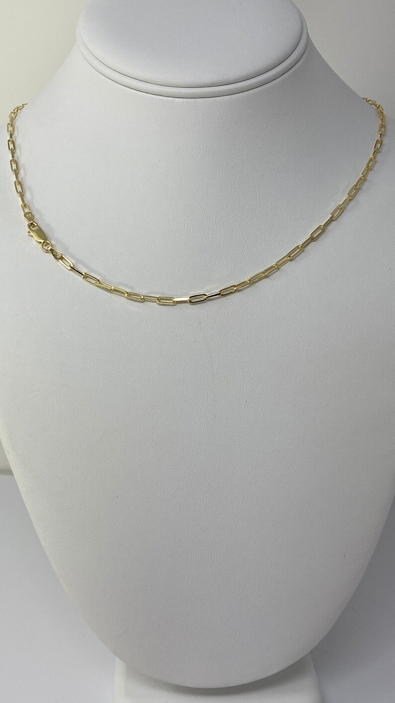 K&ouml;nnte beinhalten: Eine goldene Kettenkette mit einem einfachen, verlinkten Design. Die Kette befindet sich auf einer wei&szlig;en Mannequin-B&uuml;ste.