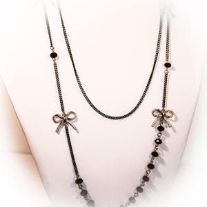 May include: A layered necklace with black beads and silver bow accents. The necklace is made of two chains, one with a delicate chain and the other with a thicker chain.