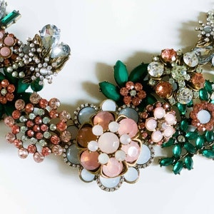 May include: A statement necklace with a floral design featuring pink, white, and green rhinestones. The necklace is made of metal and has a vintage style.
