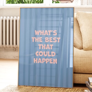 Puede incluir: Impresi&oacute;n art&iacute;stica enmarcada con un fondo a rayas azul claro y el texto rosa "WHAT'S THE BEST THAT COULD HAPPEN". La obra de arte se presenta en un marco dorado, apoyada contra un sof&aacute; beige.