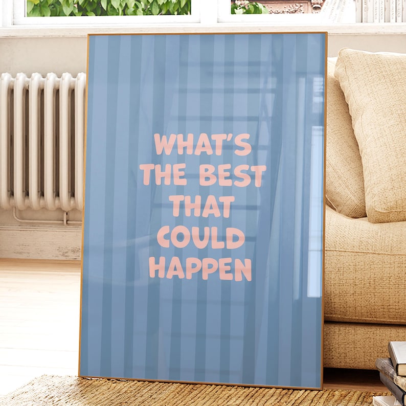 Puede incluir: Impresi&oacute;n art&iacute;stica enmarcada con un fondo a rayas azul claro y el texto rosa "WHAT'S THE BEST THAT COULD HAPPEN". La obra de arte se presenta en un marco dorado, apoyada contra un sof&aacute; beige.